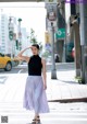 A woman in a black top and purple pleated skirt crossing the street.