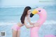 A woman in a bikini hugging a pink flamingo on the beach.