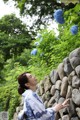 A woman in a blue and white dress leaning against a stone wall.